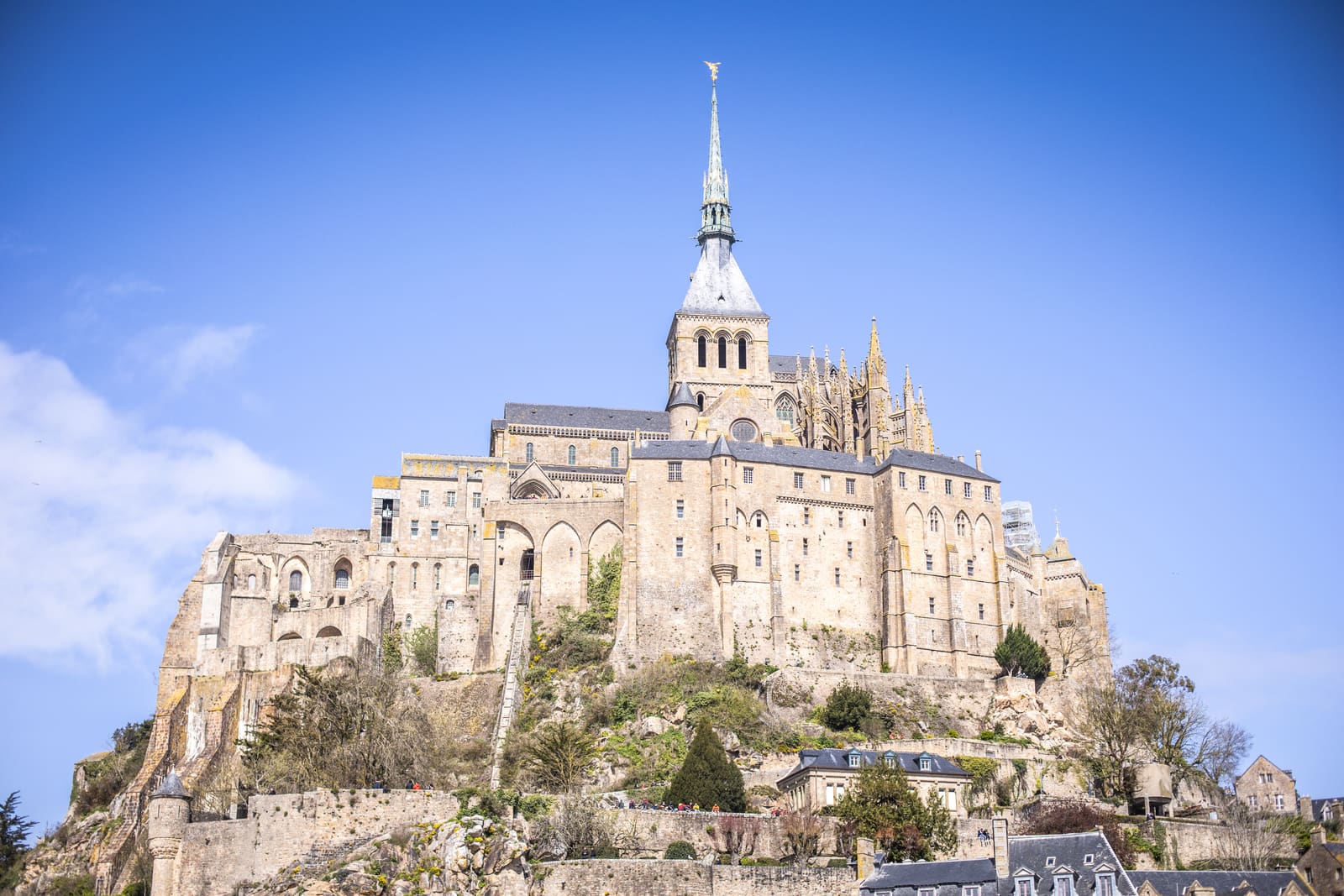 Mont Saint-Michel abbey perched dramatically on a rocky island under a bright blue sky in France.