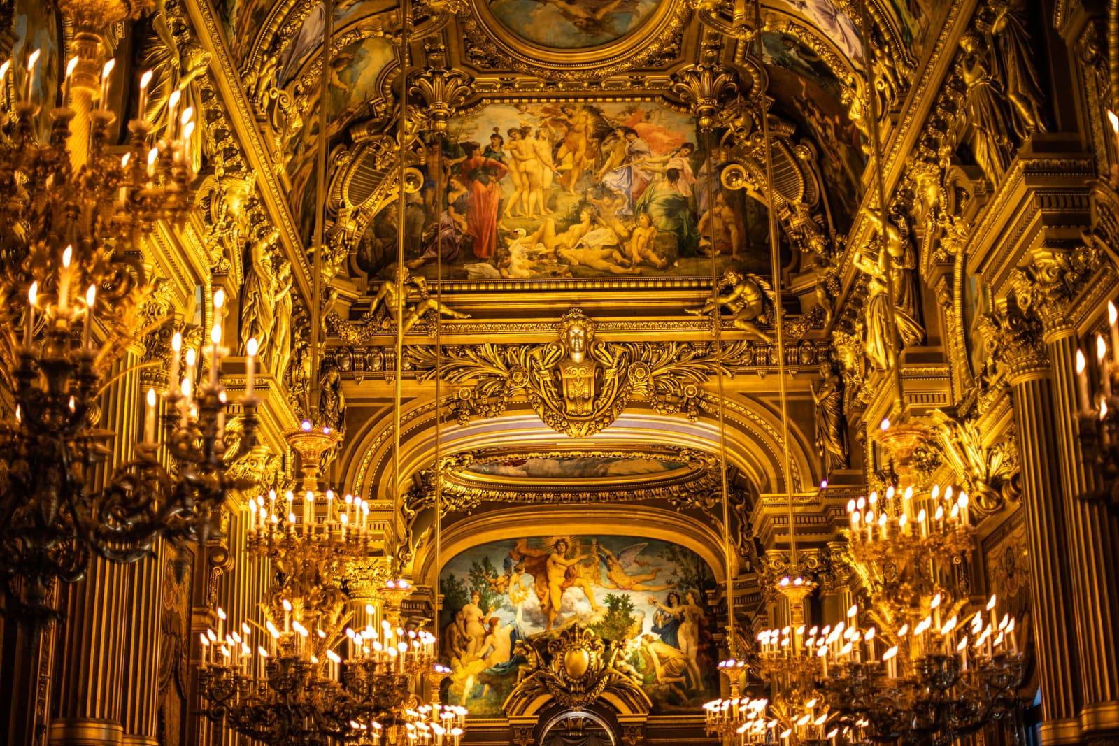 Ornate golden interior of the Paris Opera Garnier with chandeliers and elaborate ceiling murals.