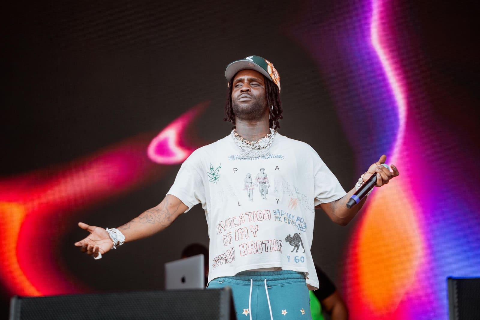 A rapper in a white tee and teal pants spreads his arms at Dreamville Festival, Raleigh, 2025