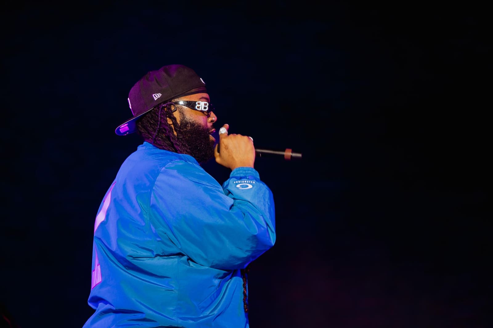 A rapper in a blue jacket and cap on a dark stage at Dreamville Festival, Raleigh, 2025