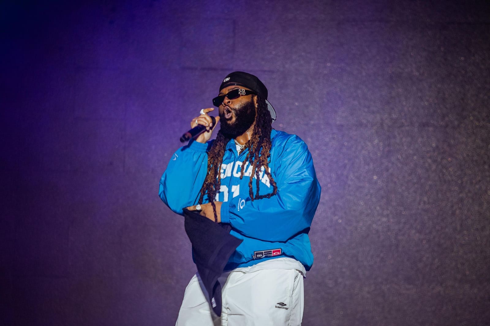 A rapper in a blue hoodie performs with a microphone at Dreamville Festival, Raleigh, 2025