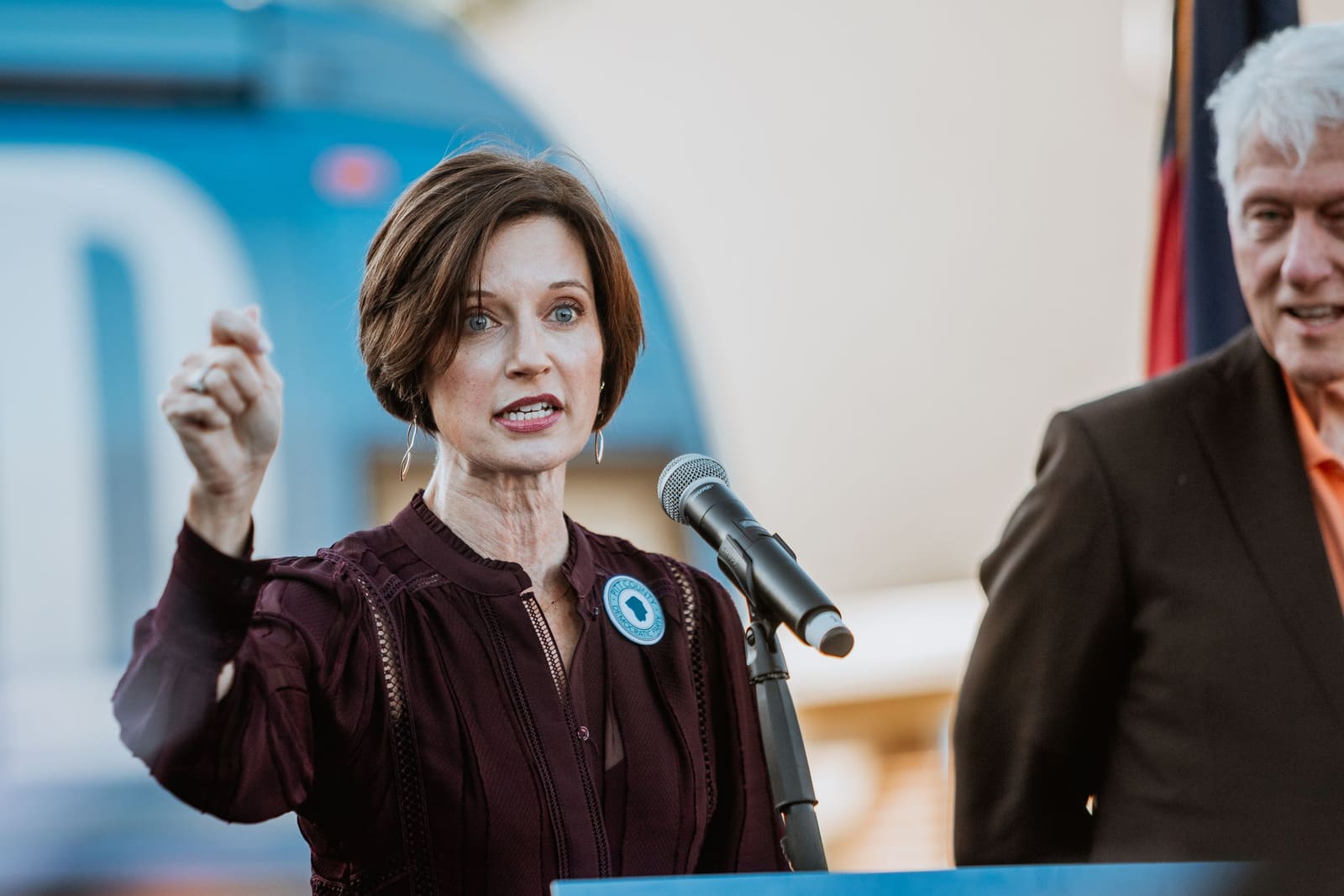 Woman in burgundy dress speaks passionately at podium during Harris campaign campaign rally event.
