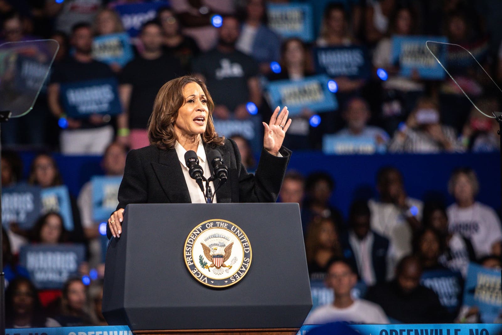 Kamala Harris raises a hand mid-speech at Minges Coliseum, Greenville, NC