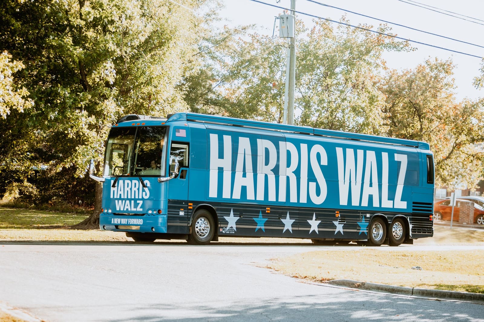 Blue Harris campaign 2024 presidential campaign bus parked on street near trees.