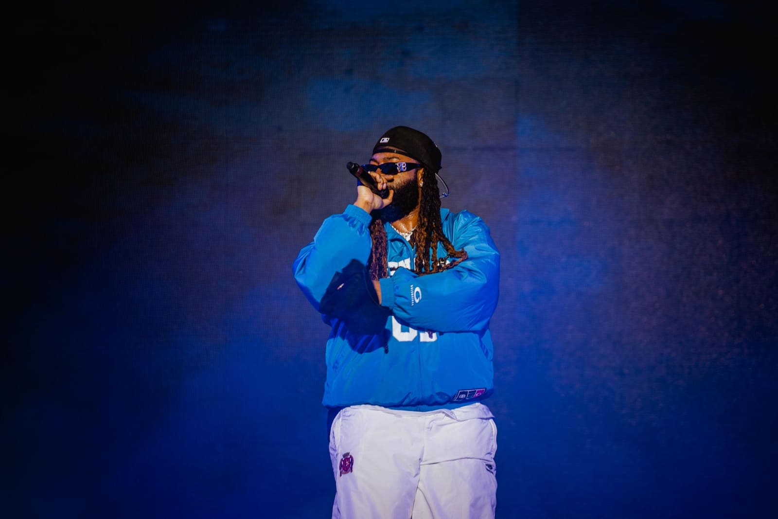 A rapper in a blue hoodie on a blue-lit stage at Dreamville Festival, Raleigh, 2025