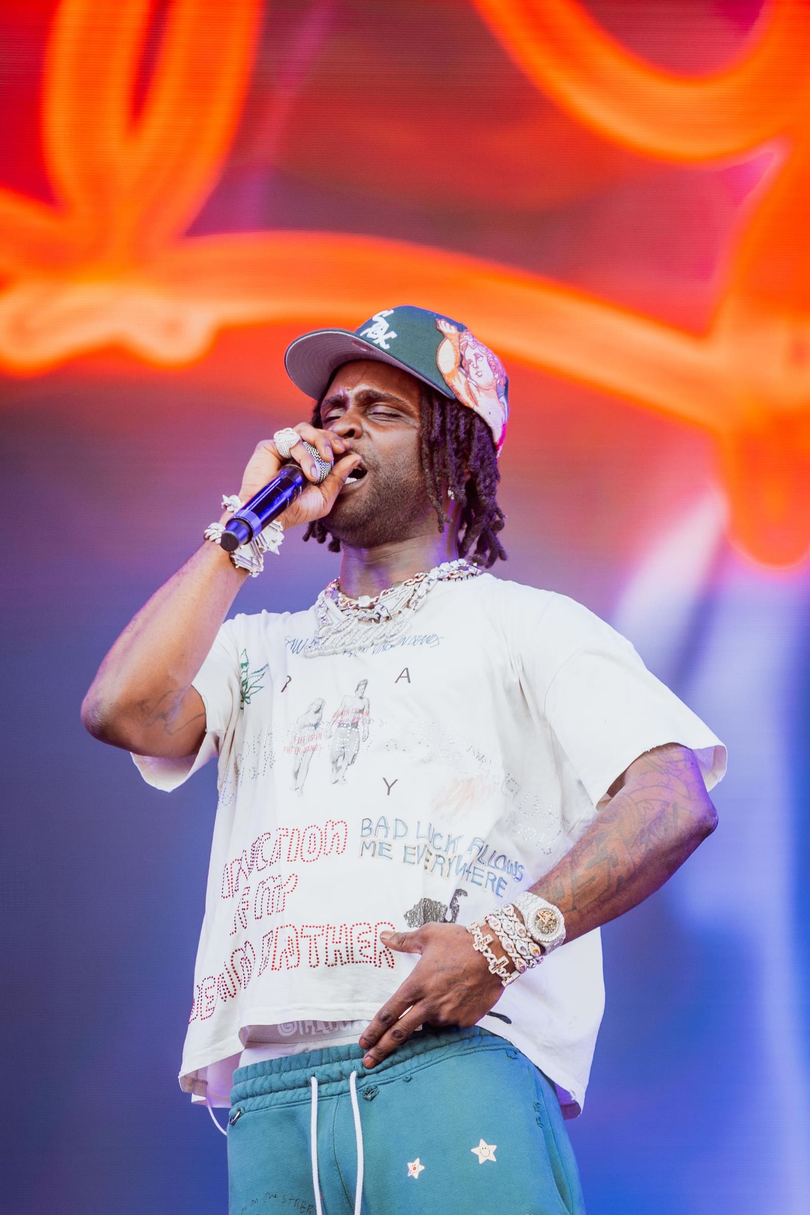 A rapper in chains performs under orange lights at Dreamville Festival, Raleigh, 2025