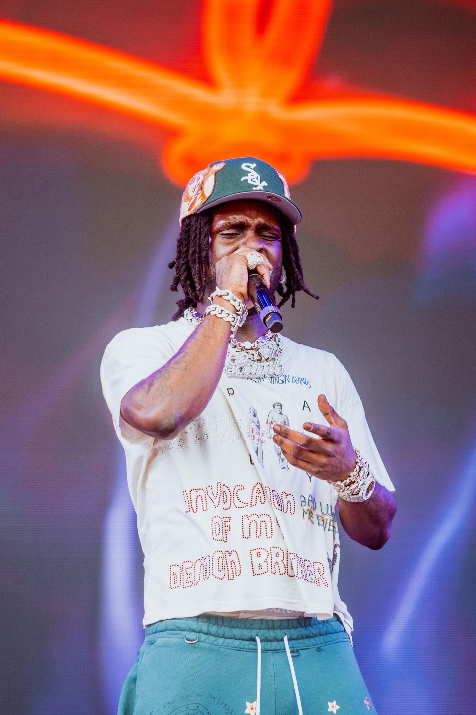 A rapper in a white tee and cap performs under neon at Dreamville Festival, Raleigh, 2025