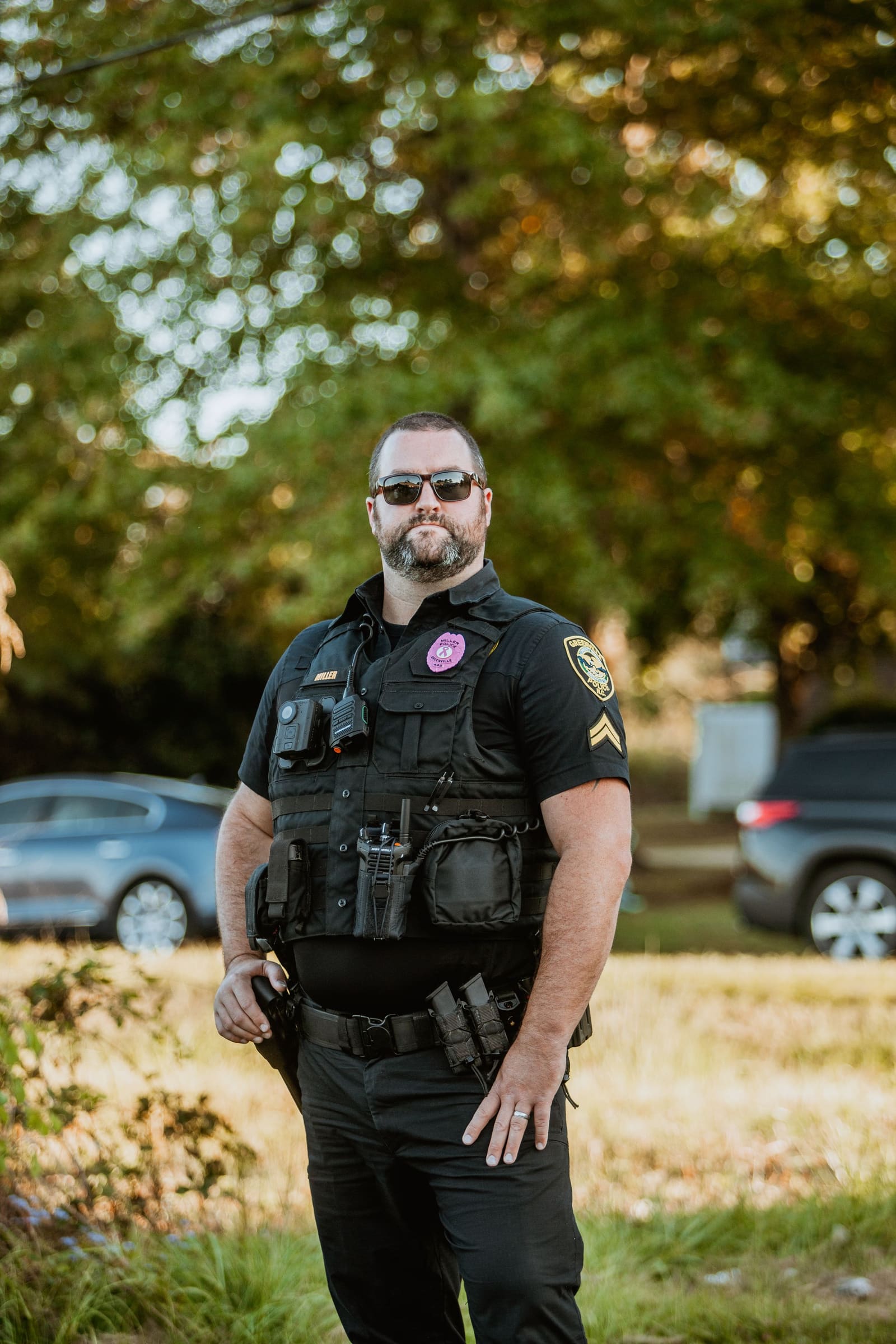 Police officer in tactical gear and sunglasses standing outdoors.