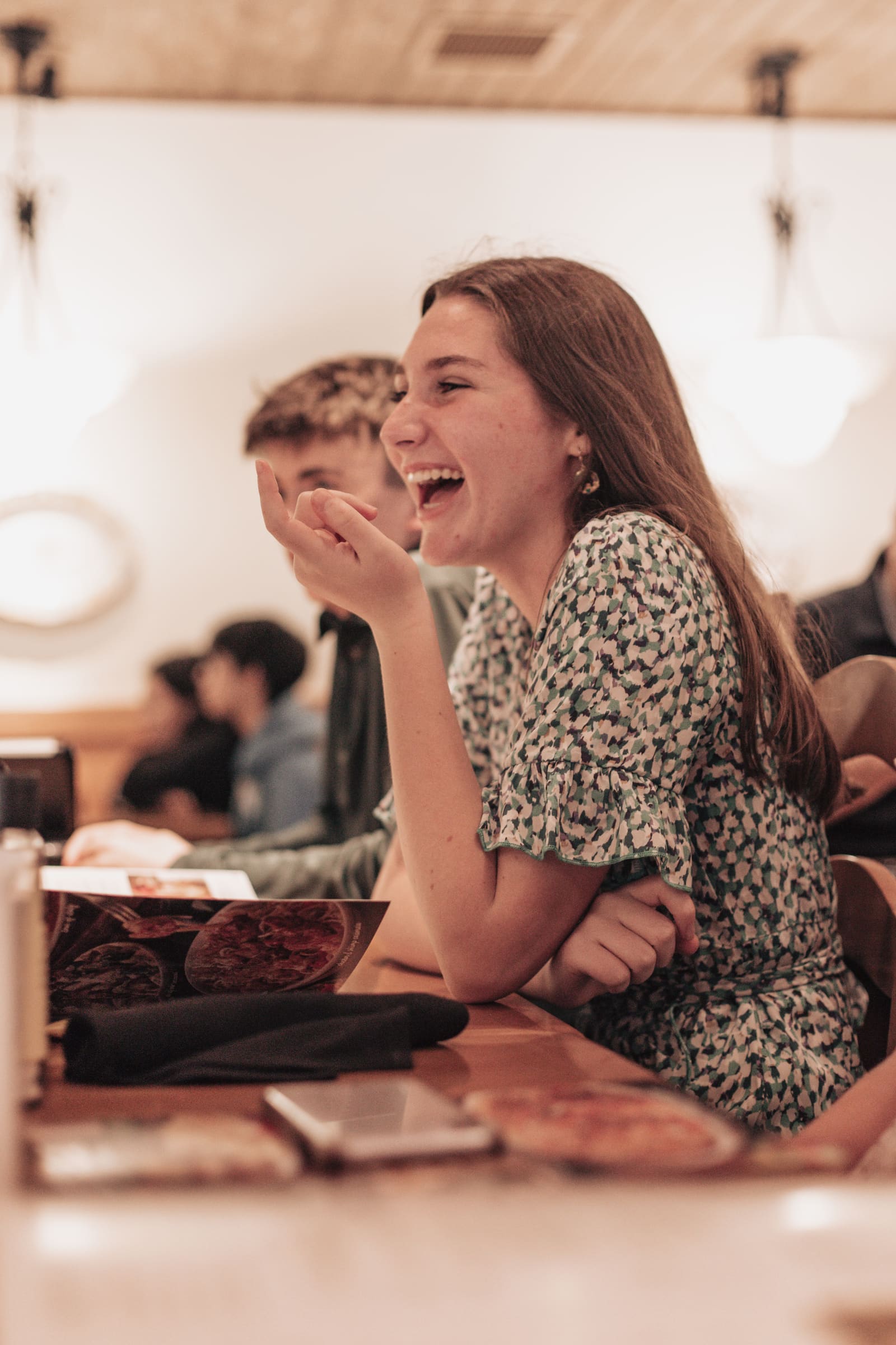 A young woman laughing at a restaurant table among friends