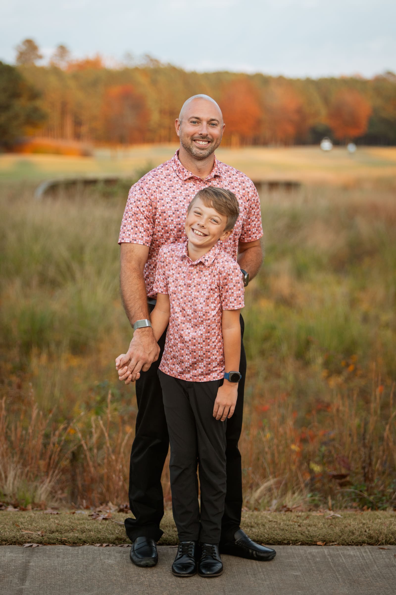 Father and son wear matching pink floral shirts posing together in autumn outdoor portrait.