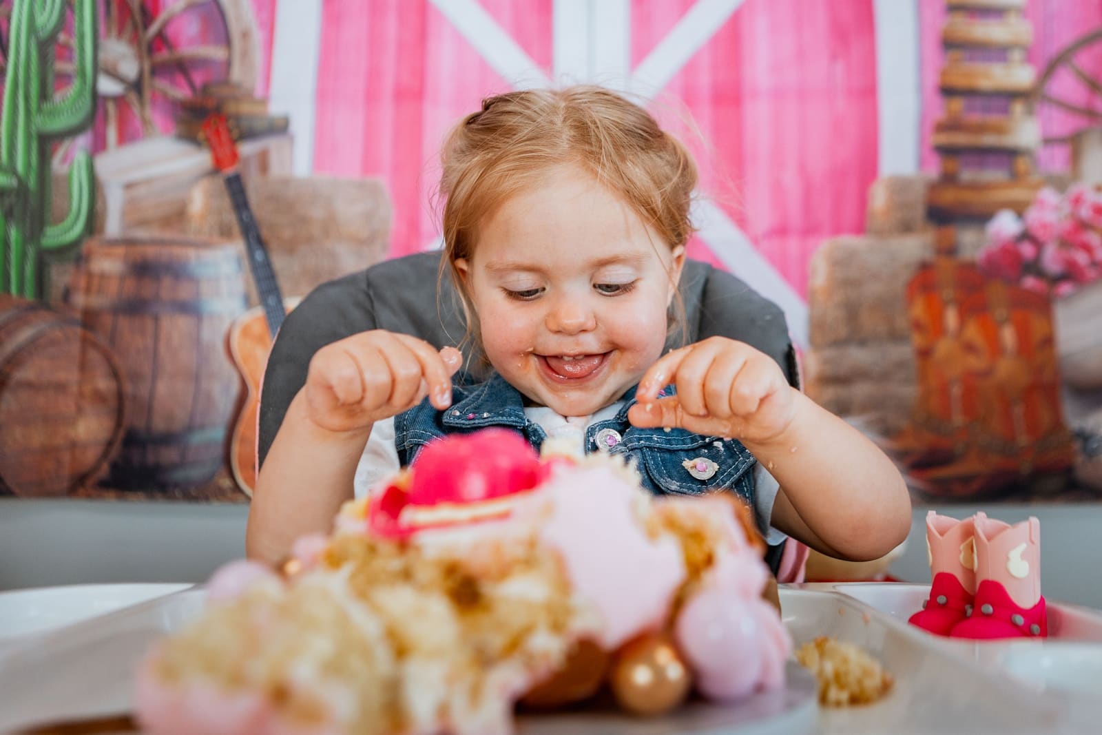 Happy toddler girl smiling while digging into a decorated cake at a birthday celebration.