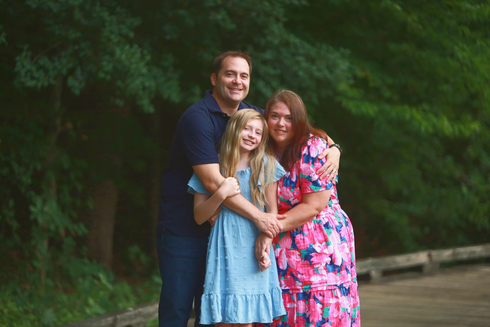A smiling family embracing each other in soft evening light beside a wooden bridge