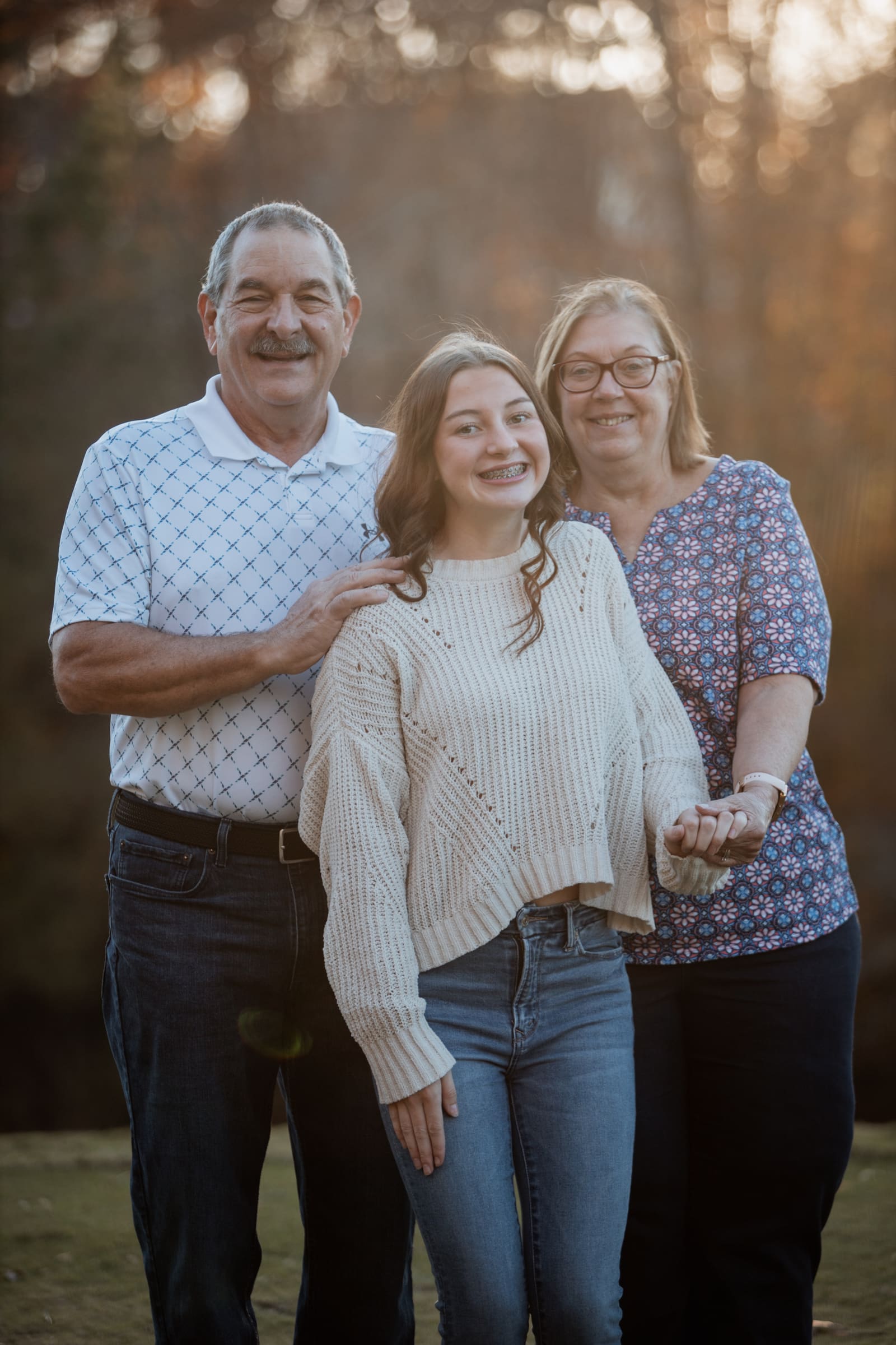 Close three-generation family portrait with warm sunset glow behind them