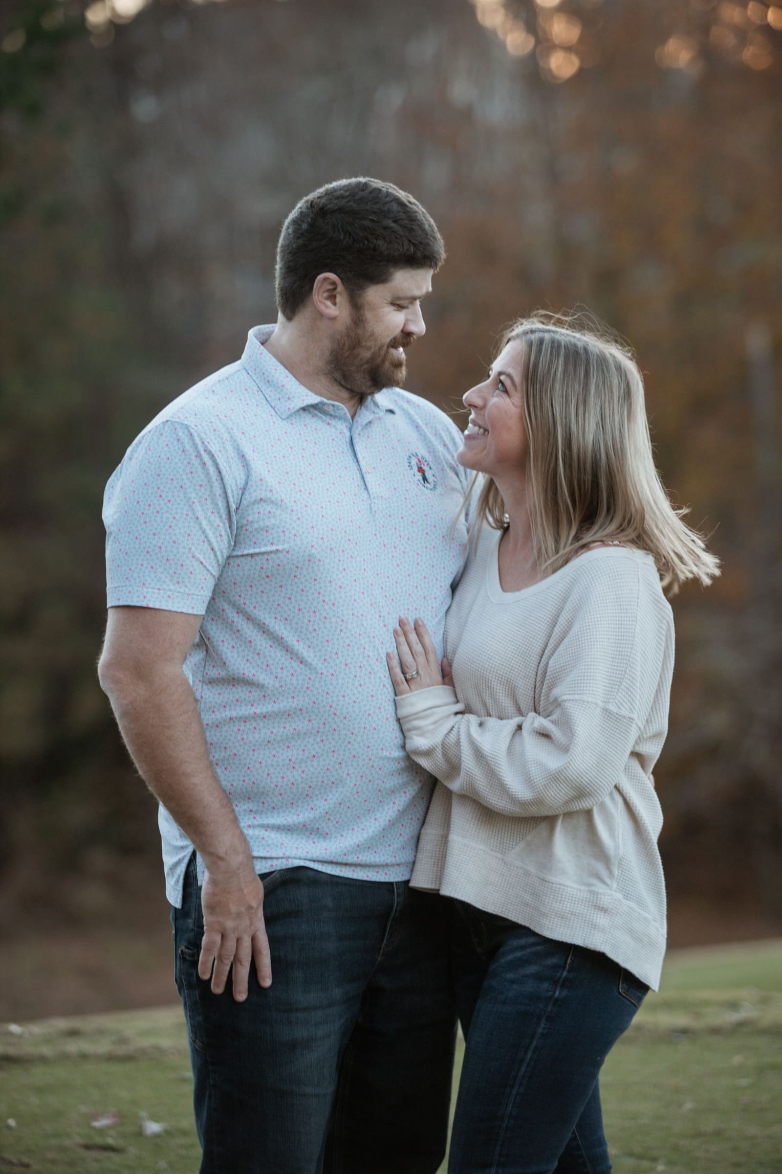 A couple laughing and embracing in warm sunset light with blurred autumn trees behind