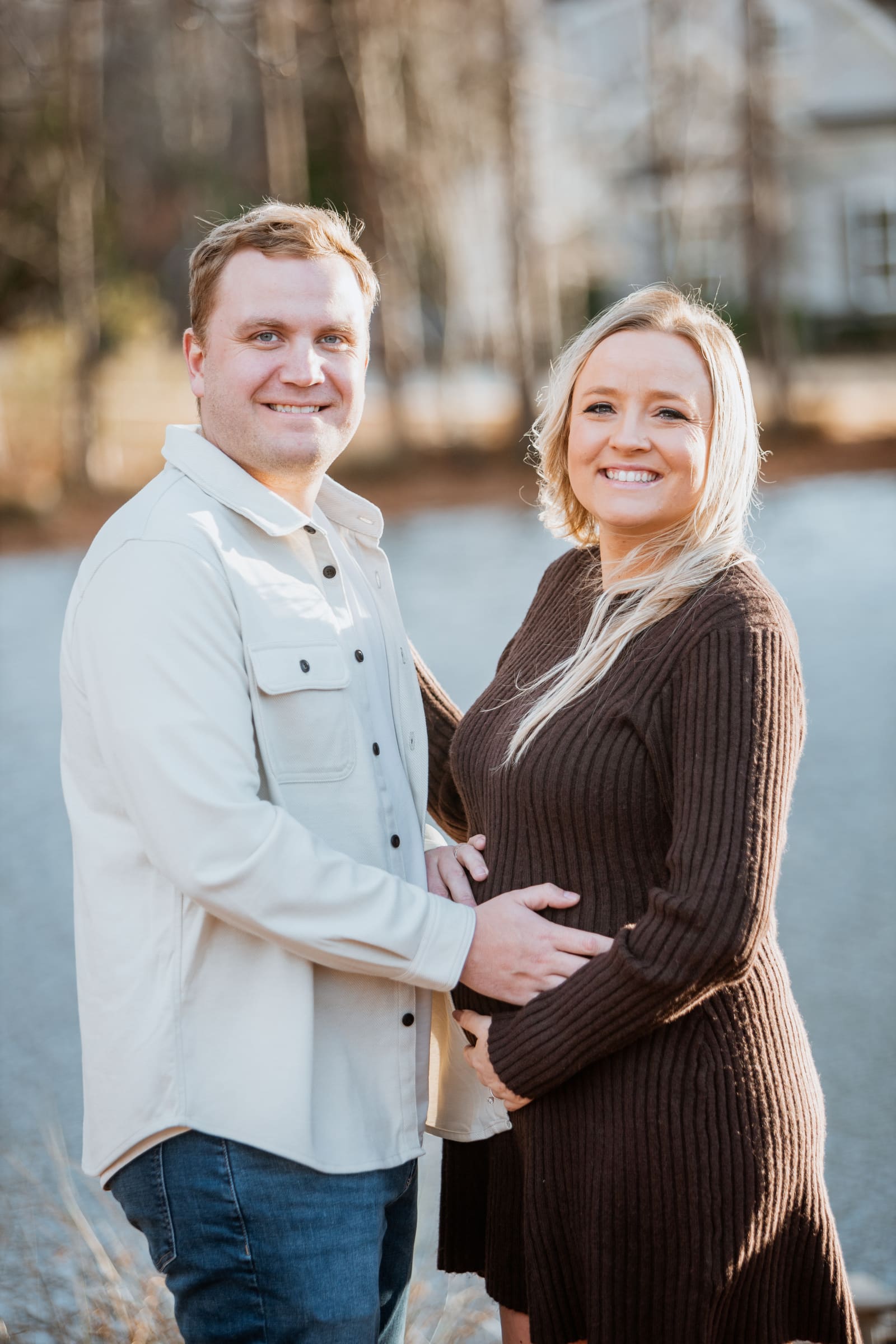 Expecting couple laughing together beside a lake in soft winter light