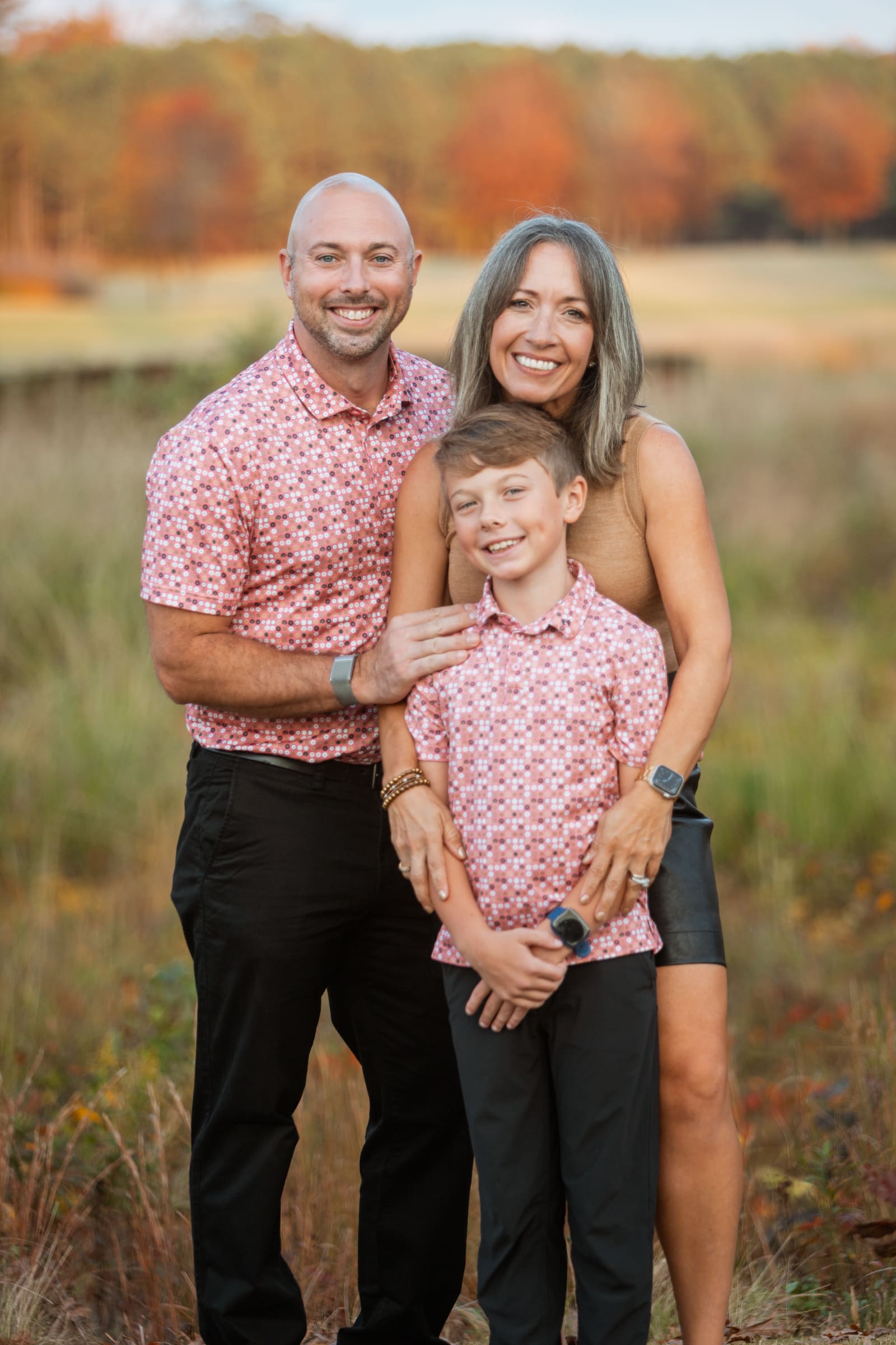A smiling couple and their son hugging close in an autumn golf course meadow