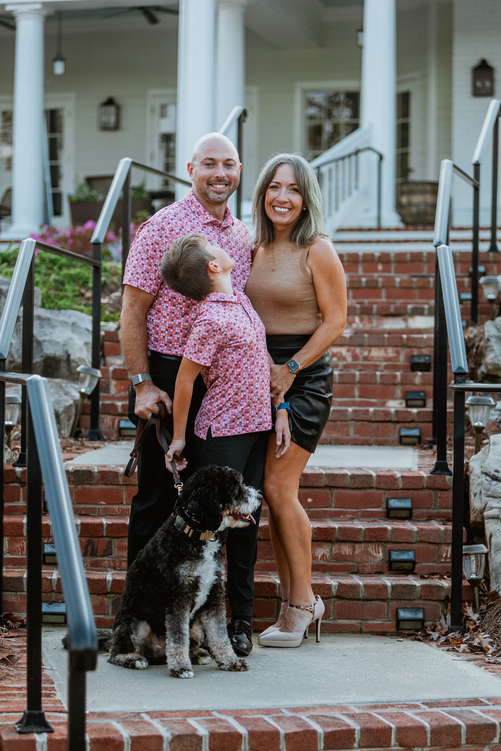 A family and their dog posed on brick steps in front of a white-columned clubhouse