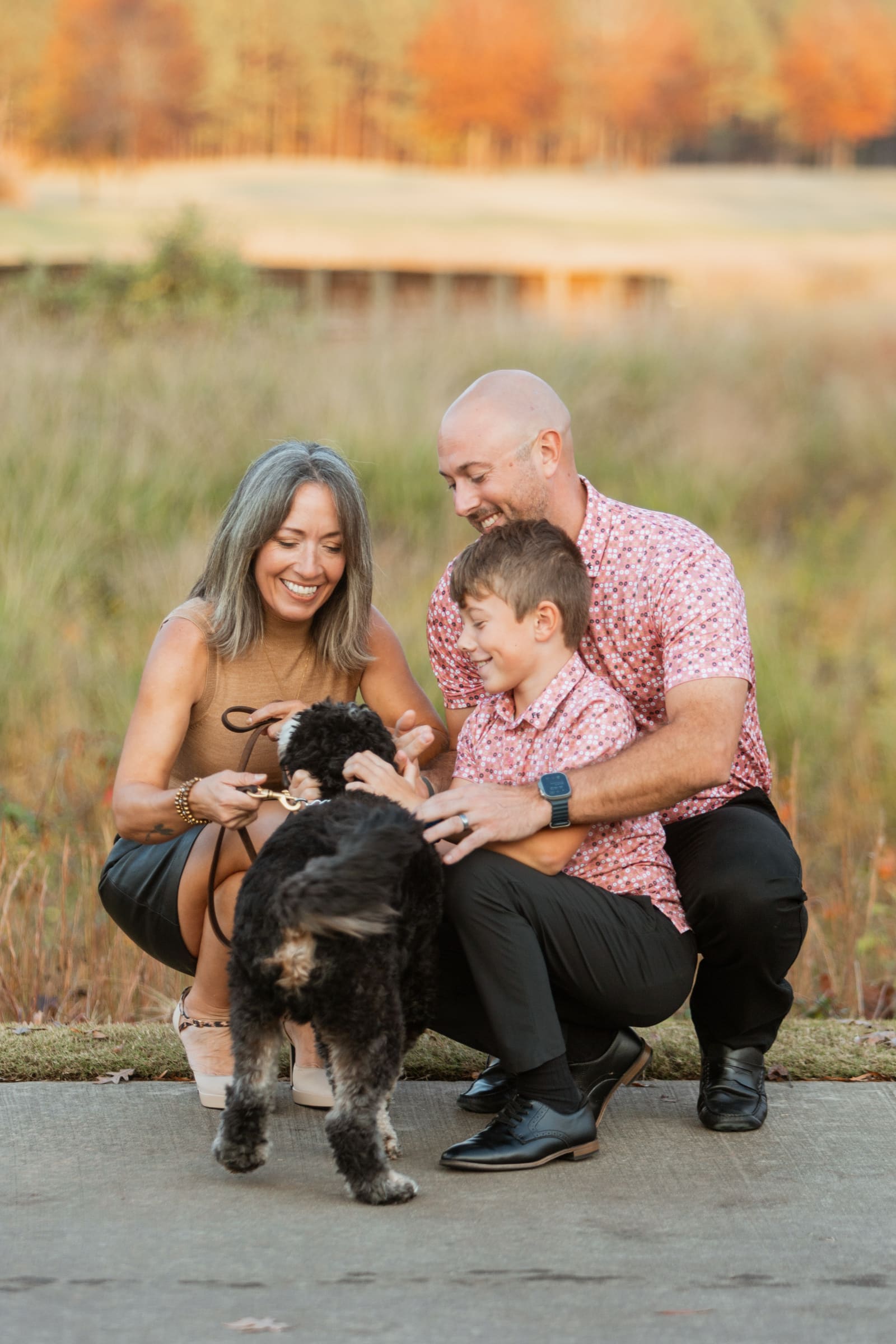 A family crouching to pet their fluffy black and white dog in an autumn meadow