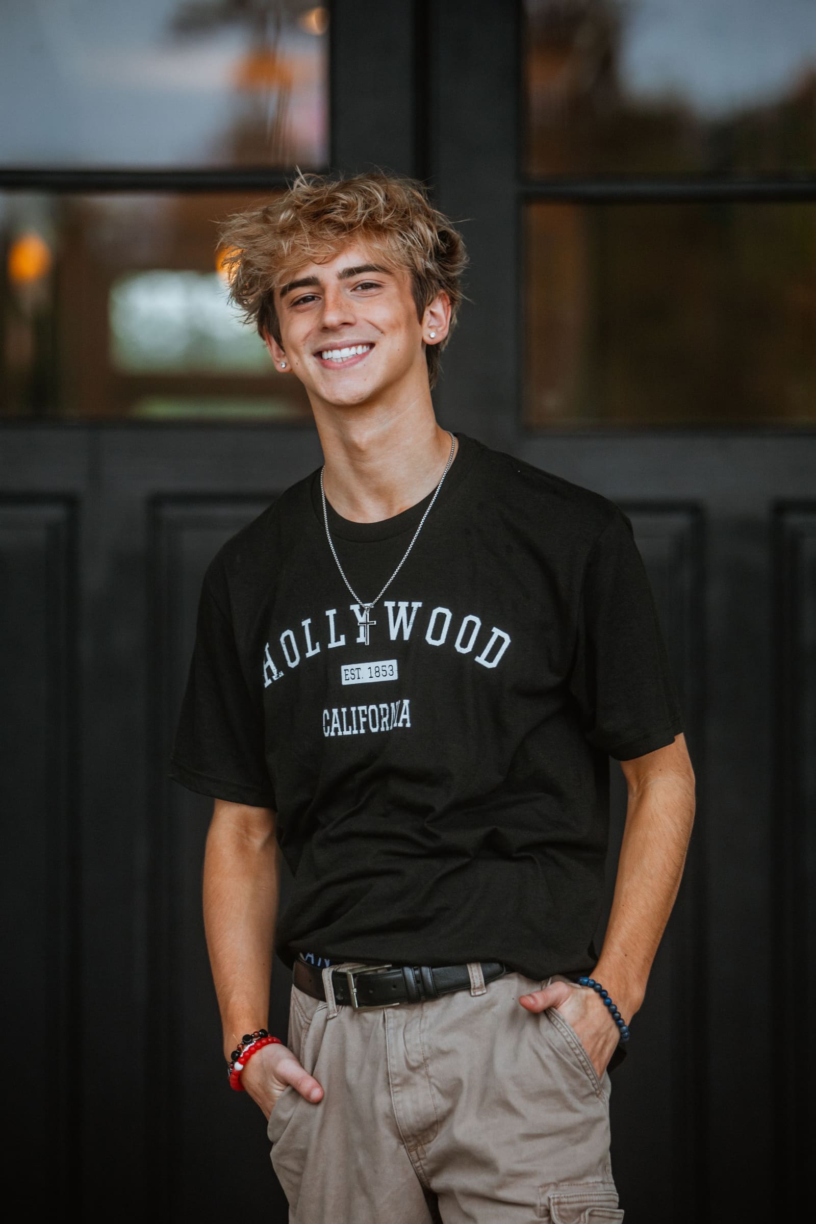 Smiling teenage boy with blonde hair in black Hollywood t-shirt standing outdoors.