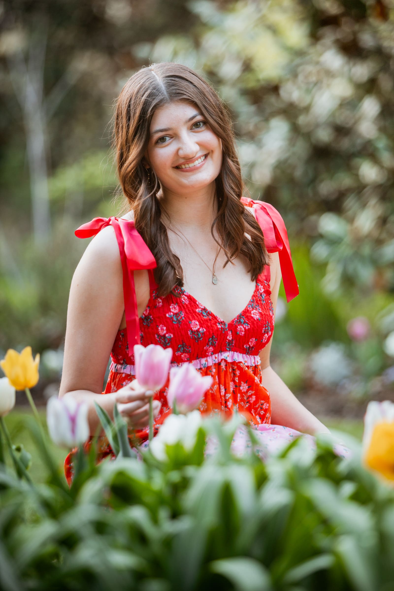 Young woman in red floral dress smiling among colorful tulips in a garden.