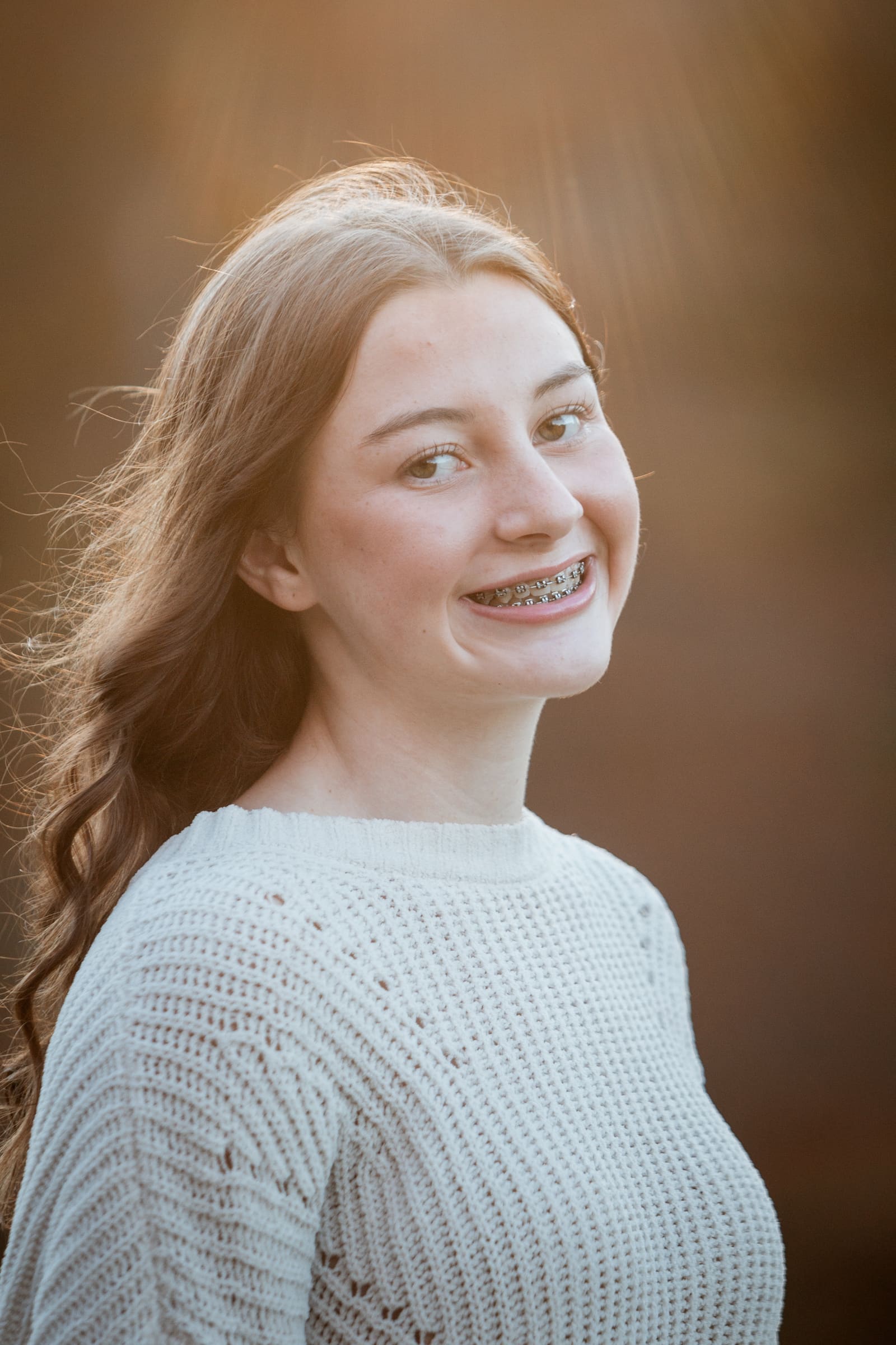 Close portrait of a smiling teenage girl in a cream sweater with a glowing golden background