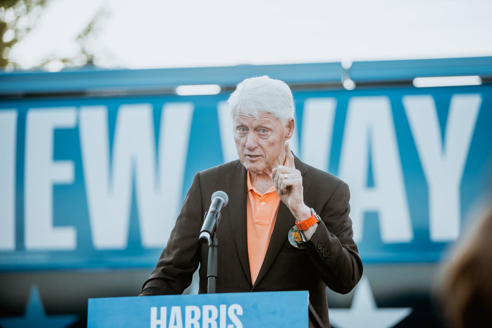 Bill Clinton gesturing at a Harris campaign lectern