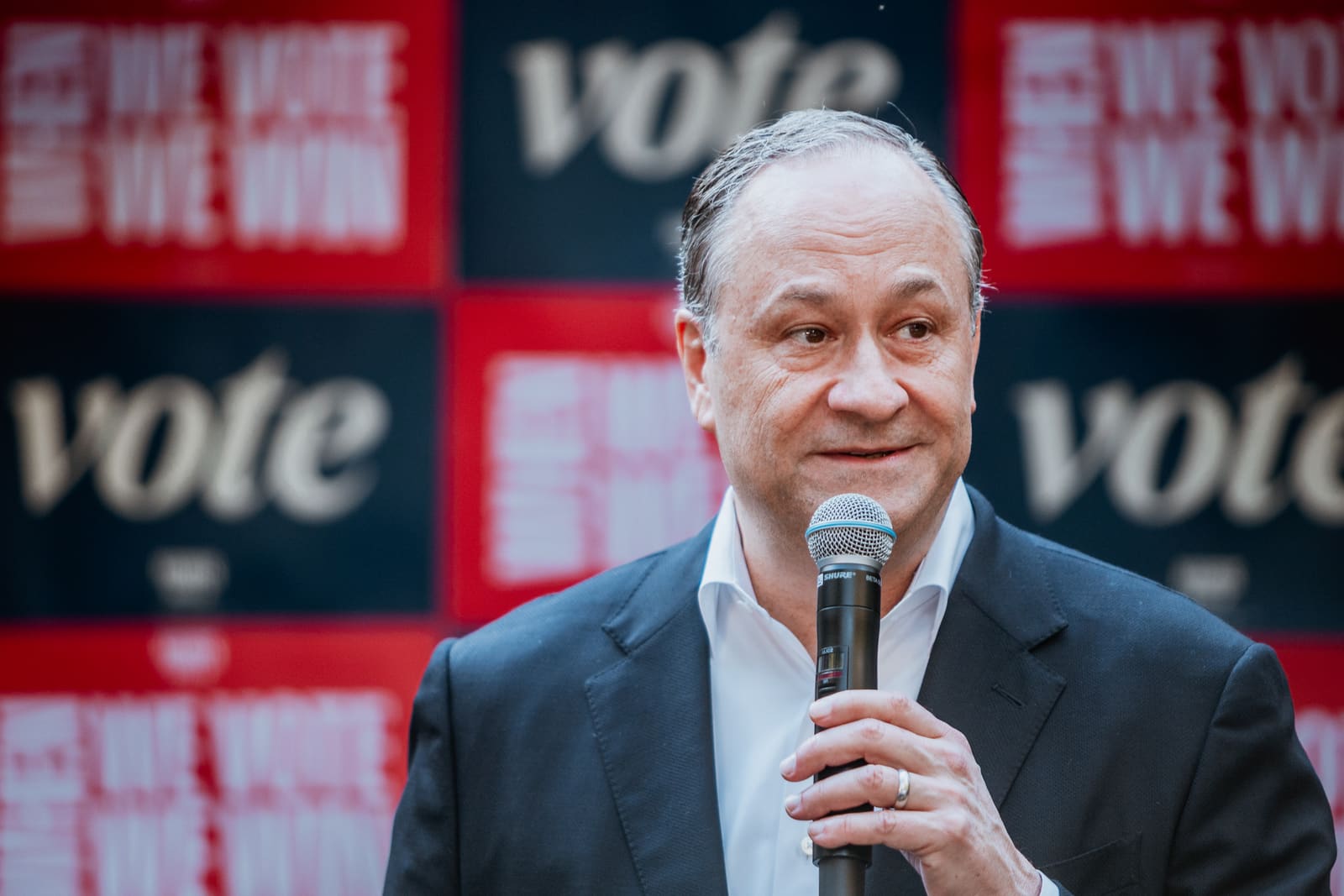 Doug Emhoff speaking into a microphone in front of Vote signs