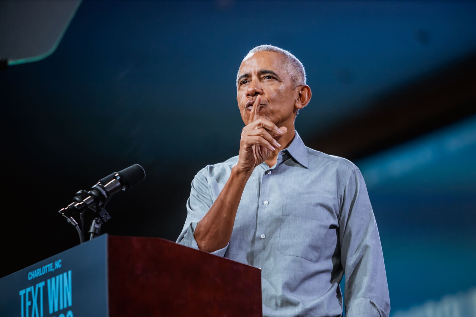 Barack Obama with a finger to his lips at the podium