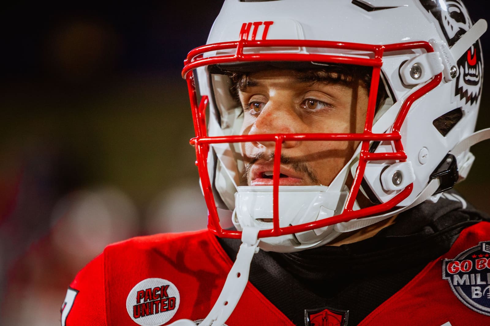 NC State Wolfpack football player in red helmet and uniform with face visible through visor during night game.