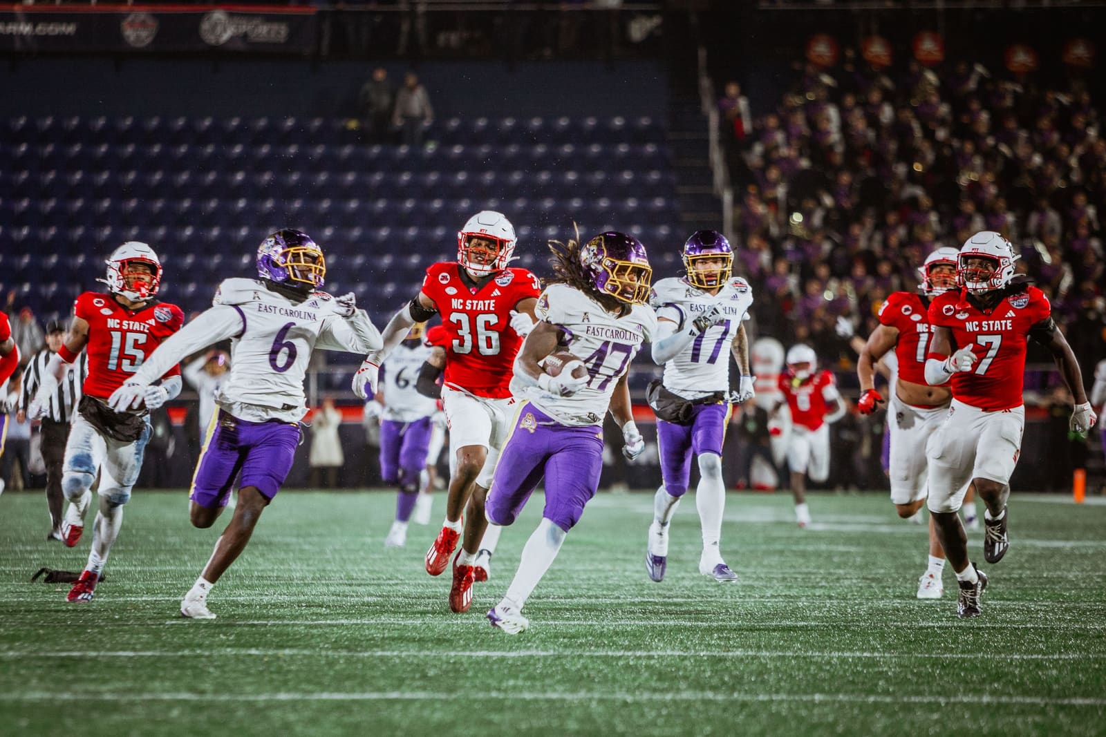ECU Pirates football player #36 runs with the ball during a night game against a team in purple uniforms.
