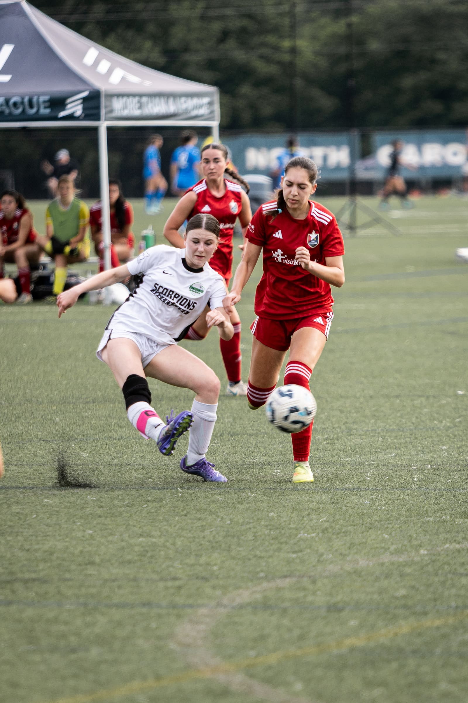 Scorpions female soccer player strikes ball while red-uniformed opponent closes in during competitive match.