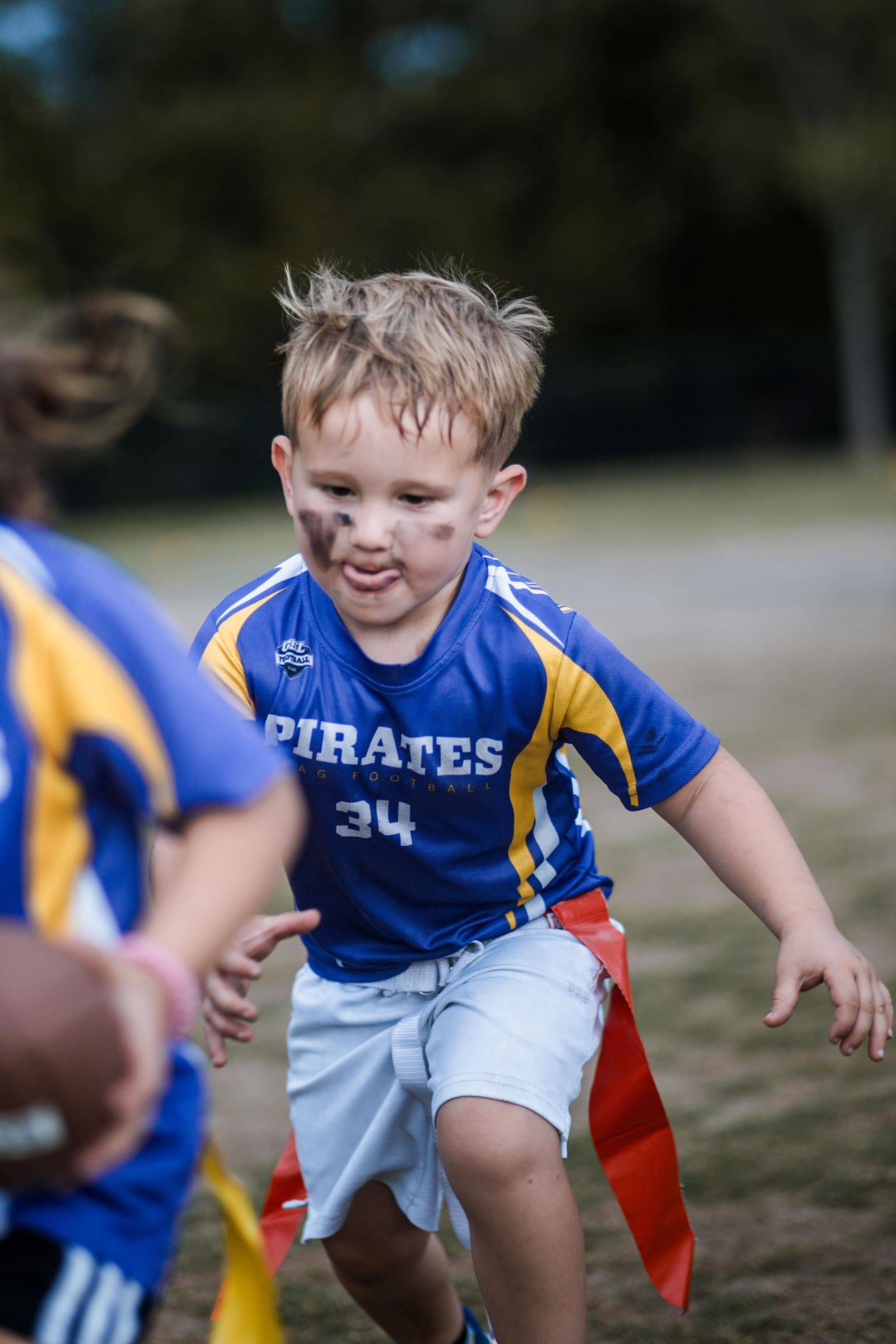 Young boy number 34 in blue Pirates jersey running with flag football flags.