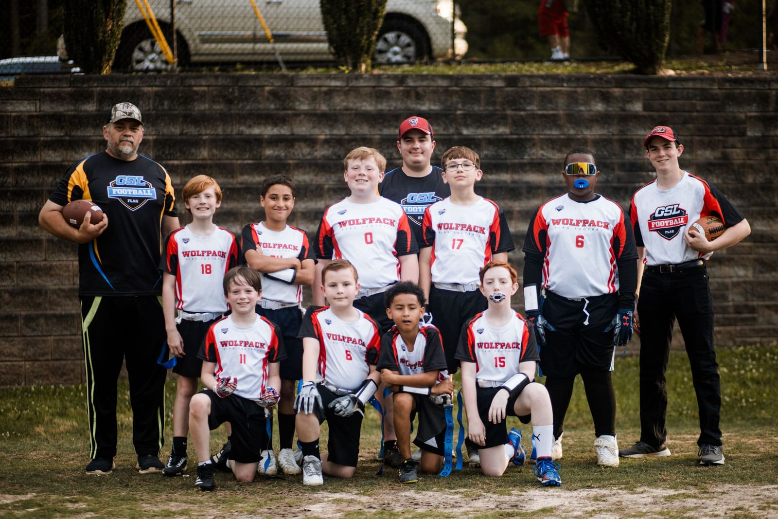 Youth baseball team in red and white Wolfpack uniforms posing with coaches on a dirt field.