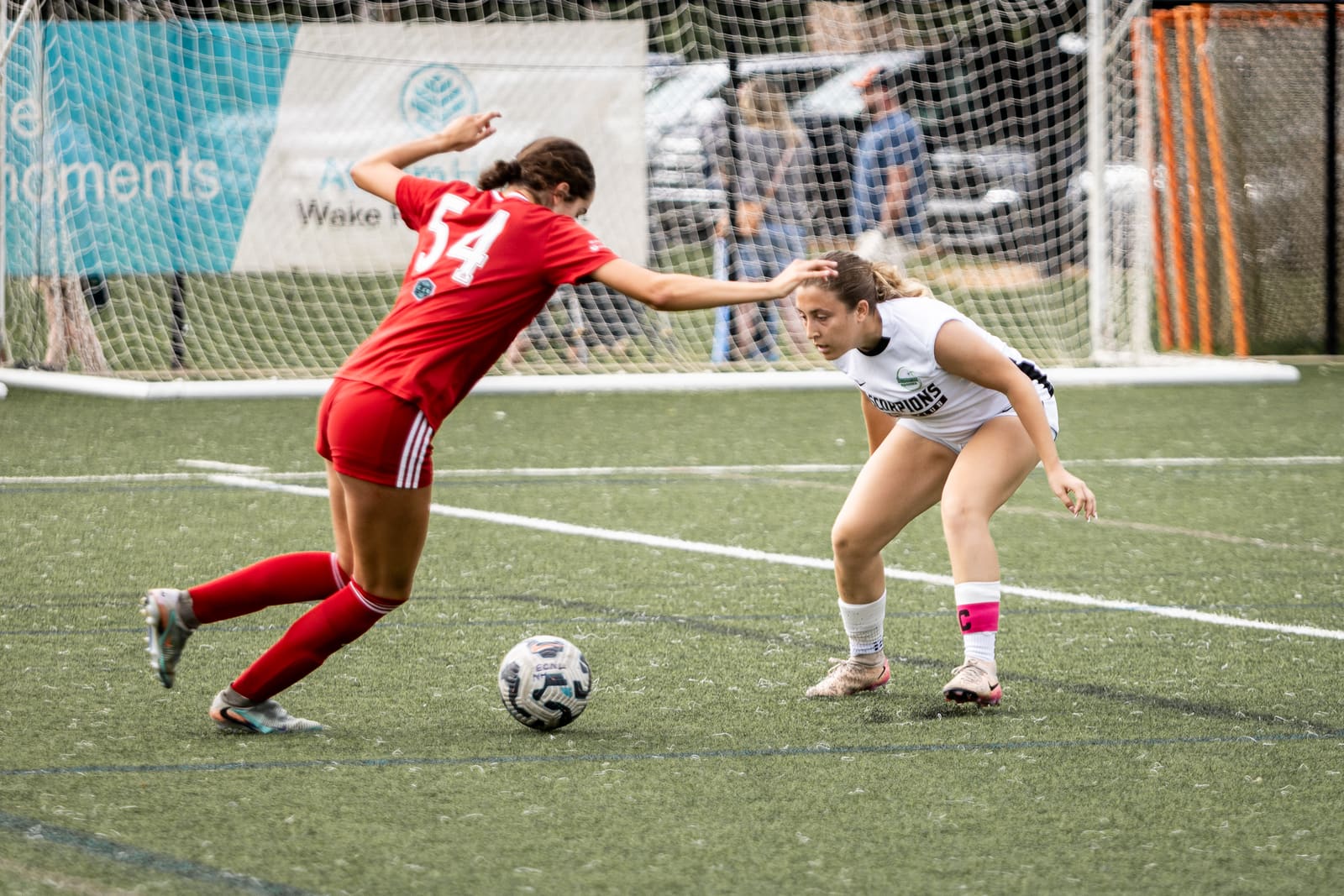 A youth girls soccer player in white dribbles past a defender in red during a match